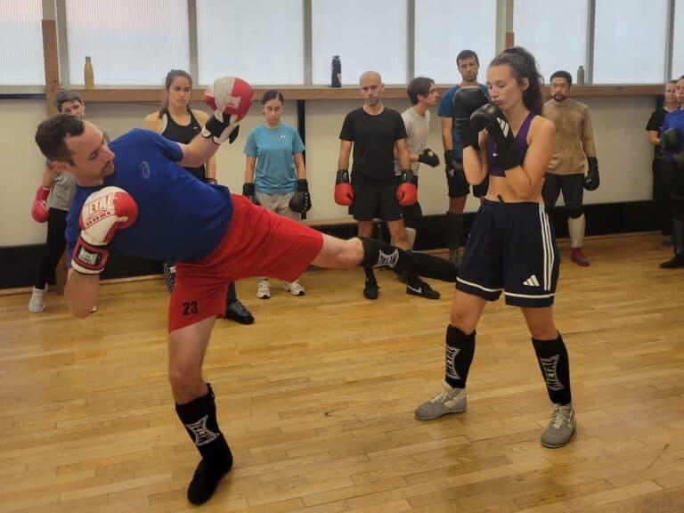 Joseph, coach du Punchistes Savate Club, montre un fouetté bas sur Louise avant l’exercice.